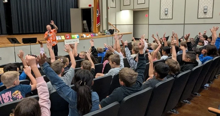 Tom Catalano presenting to a full school auditorium, students with hands raised