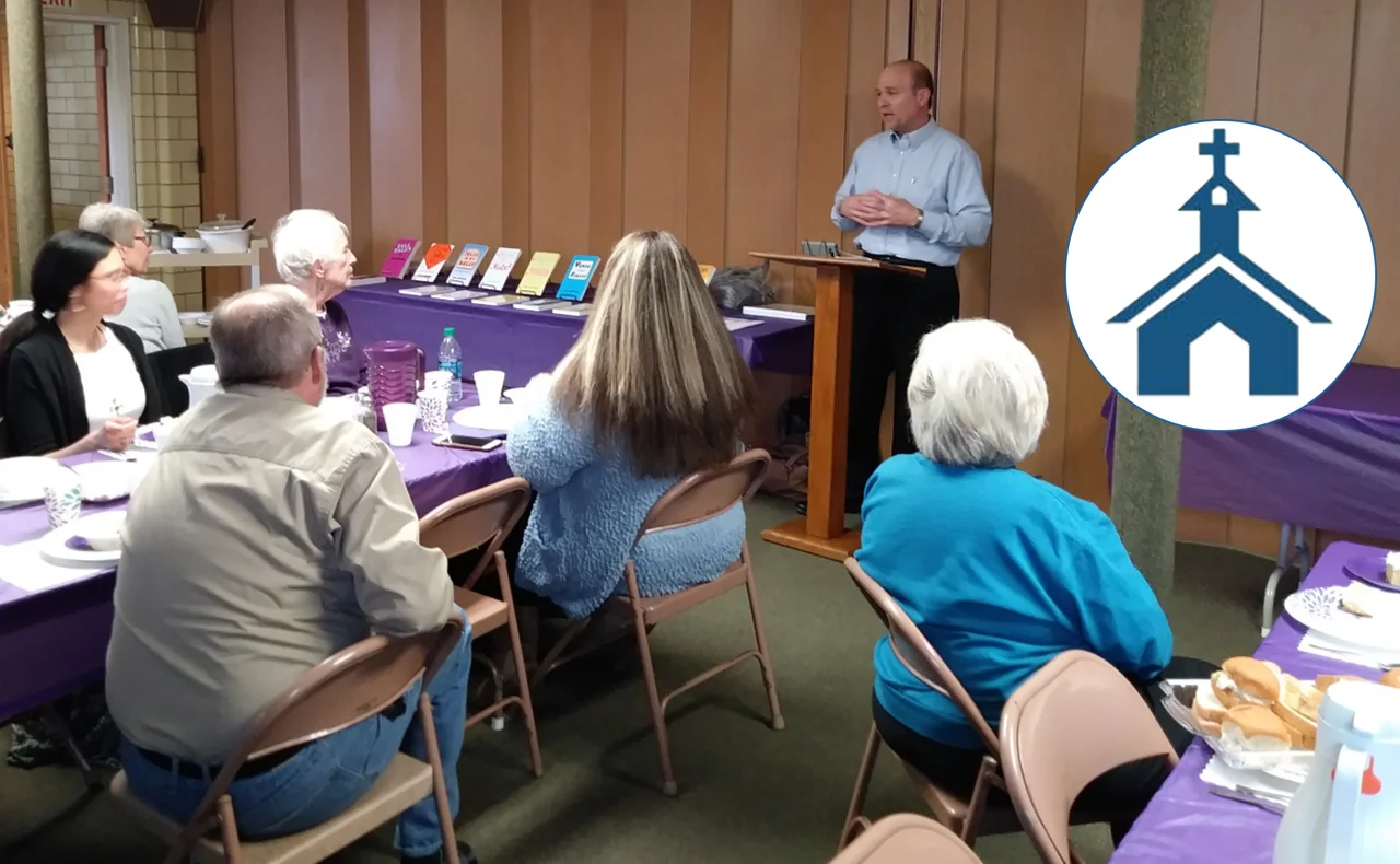 Tom Catalano speaking to a church fellowship group, with the church's logo
